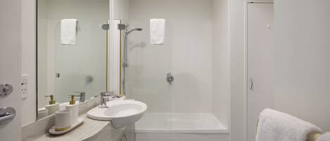 A bathroom with a sink, mirror, shower, and toilet.