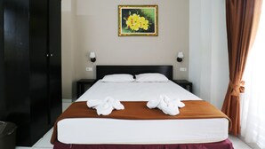 A hotel room with a large bed, two pillows, a brown headboard, a painting on the wall, a nightstand, a lamp, and a curtain. - Warapsari Inn (Kuta)