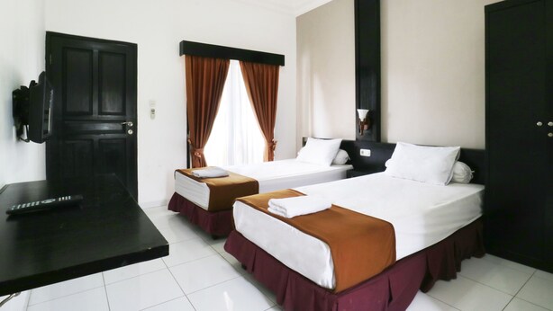 A hotel room with two beds, a desk, a TV, and a window with curtains. - Warapsari Inn (Kuta)