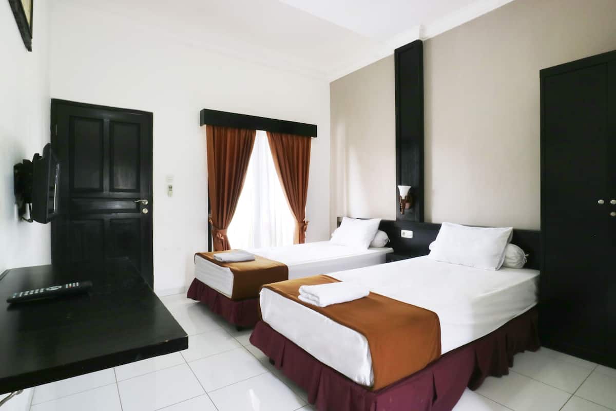 A hotel room with two beds, a desk, a TV, and a window with curtains.