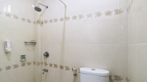 A bathroom with a shower, toilet, and a small shelf with toiletries. - Warapsari Inn (Kuta)