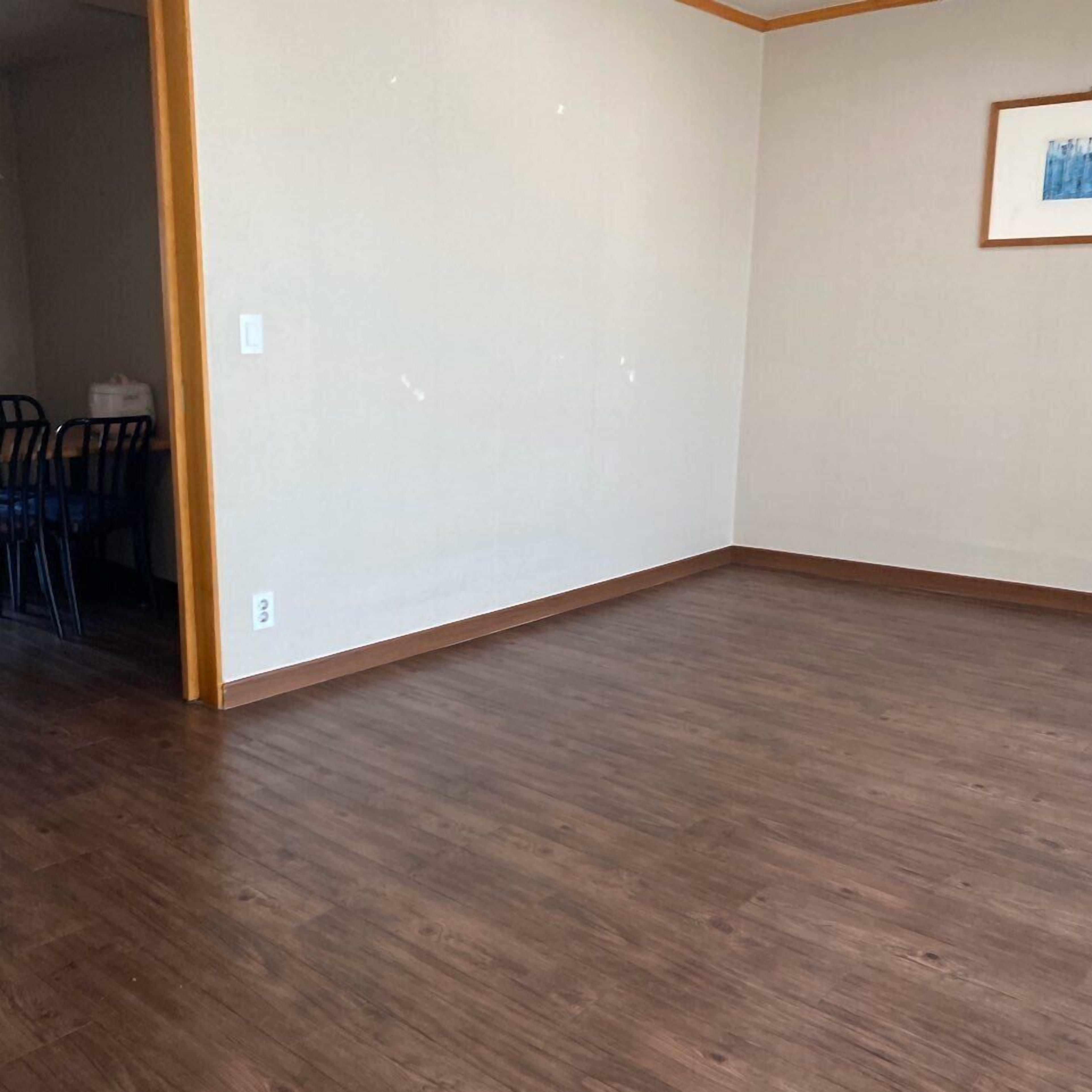 Una habitación con piso de madera, pared blanca y un cuadro enmarcado.