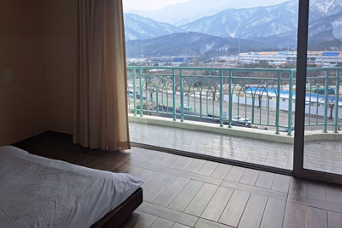 A hotel room with a bed, a view of mountains, and a balcony with a railing.
