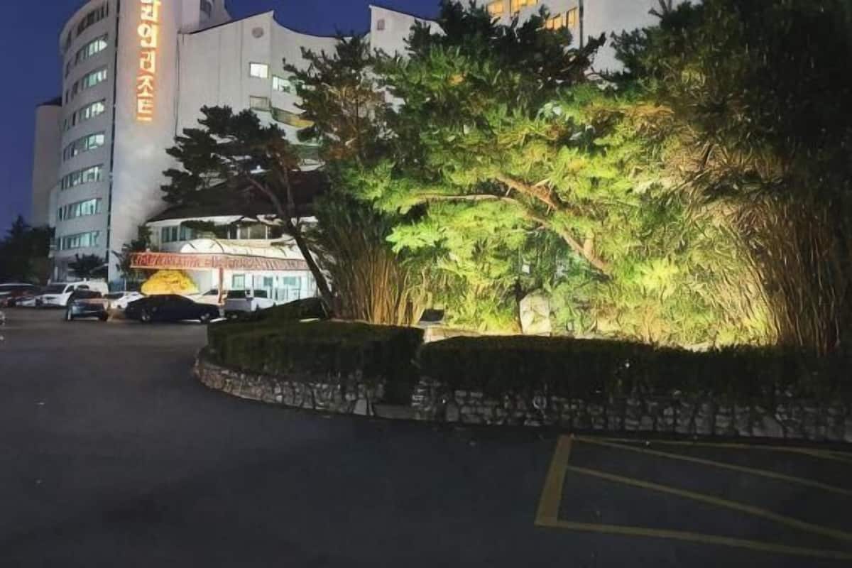 A hotel with a parking lot, a building with a sign, and a landscaped area with trees.