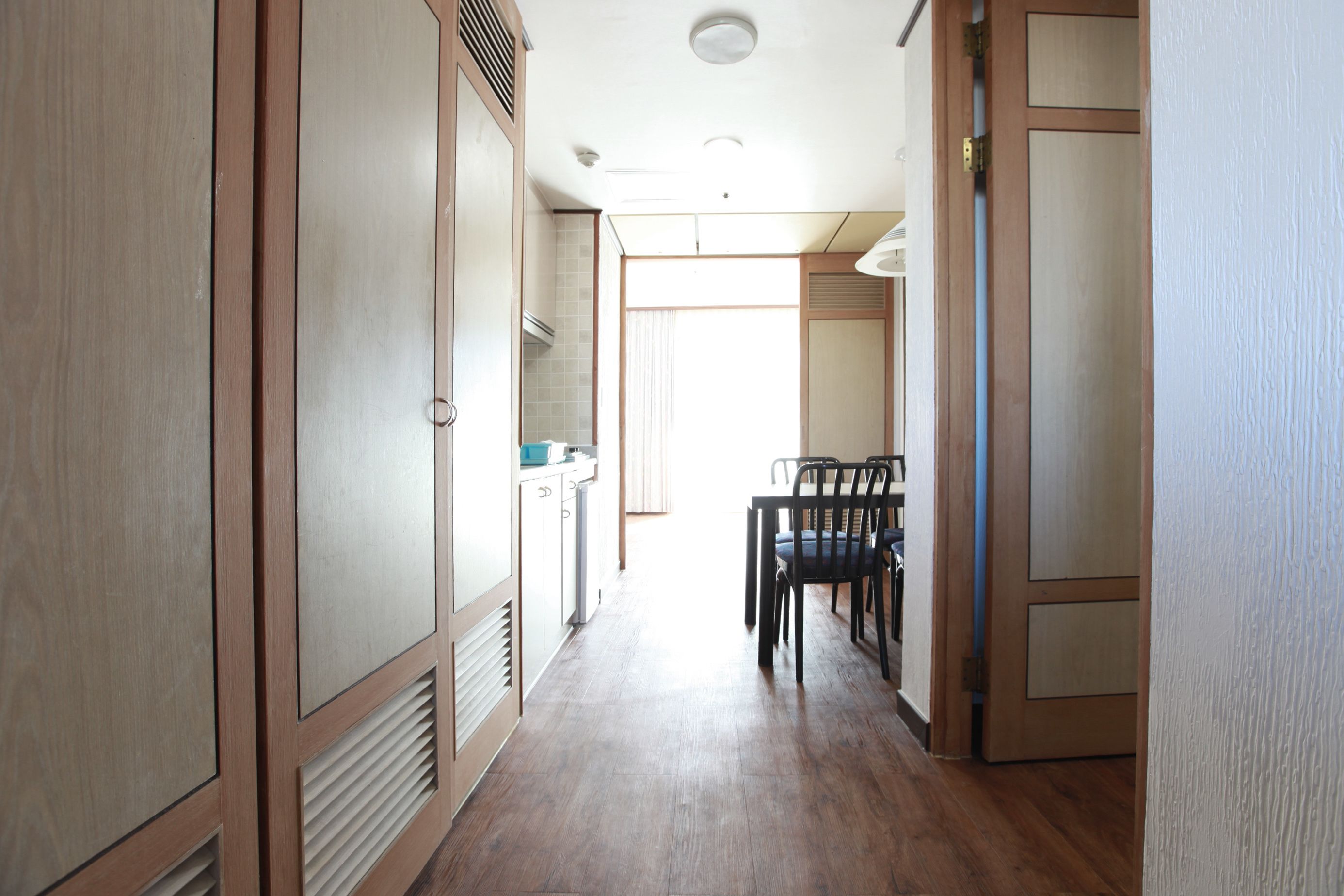 Un pasillo estrecho con suelo de madera, una mesa de comedor con sillas y una zona de cocina con armarios y una estufa.
