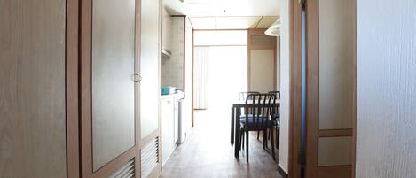 Un pasillo estrecho con suelo de madera, una mesa de comedor con sillas y una zona de cocina con armarios y una estufa.