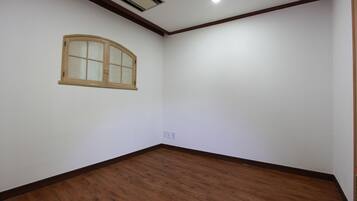 Una habitación con suelo de madera, paredes blancas, ventana con marco de madera y una lámpara empotrada en el techo.