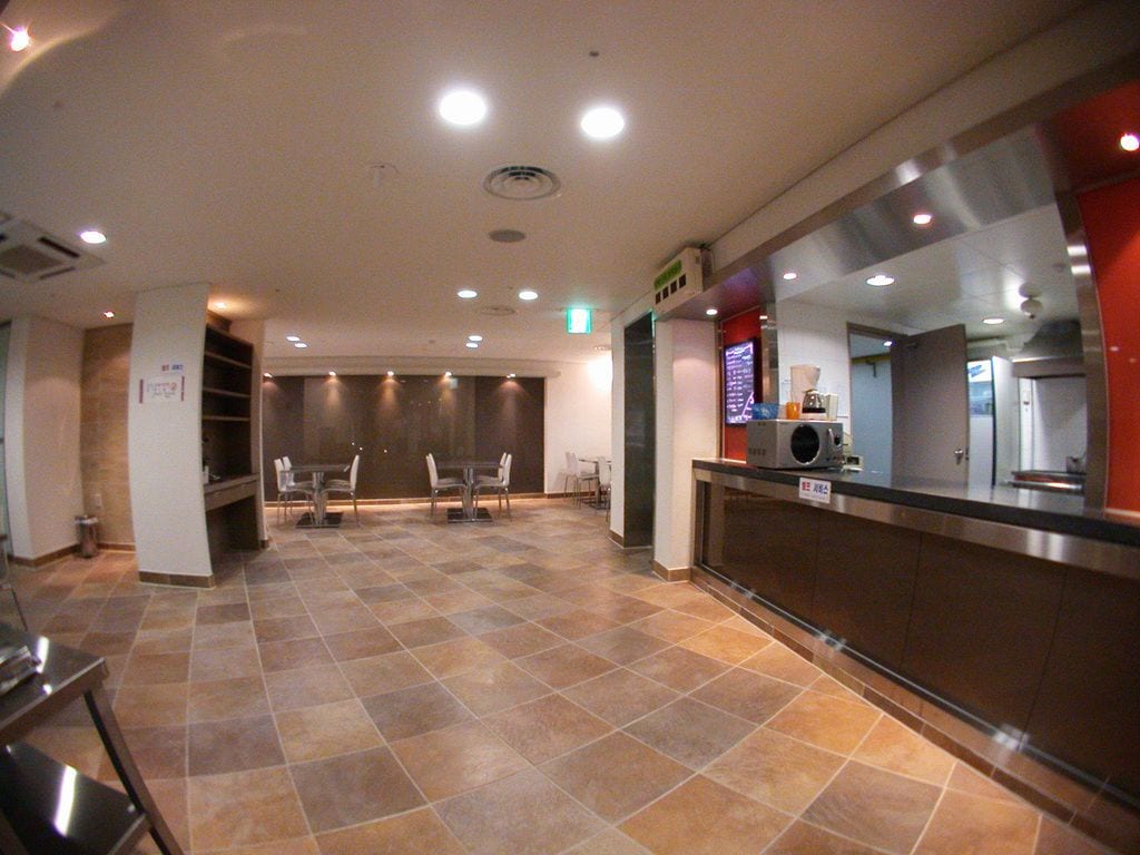 A spacious lobby with a tiled floor, a reception desk, and a seating area with tables and chairs.