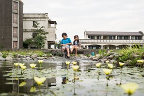 A man and a child playing in a water feature with a pond and rocks, surrounded by buildings. - Fly Inn Yilan (Dongshan)