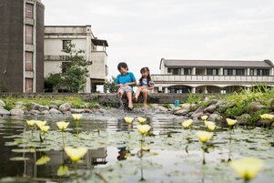 Un hombre y un niño juegan en una fuente de agua con un estanque y rocas, rodeado de edificios.