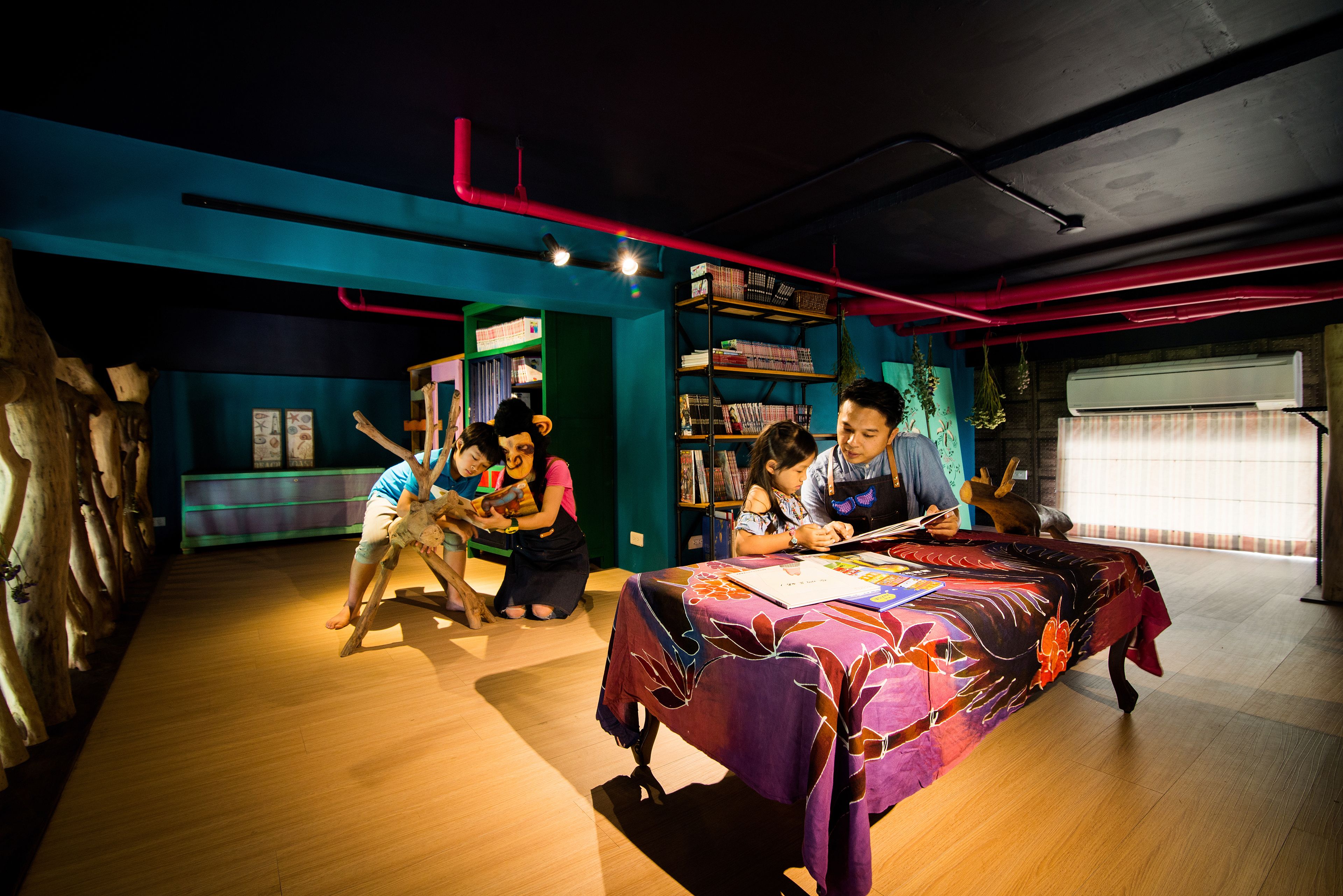 A room with a wooden floor, a table with a colorful tablecloth, and a bookshelf filled with books.