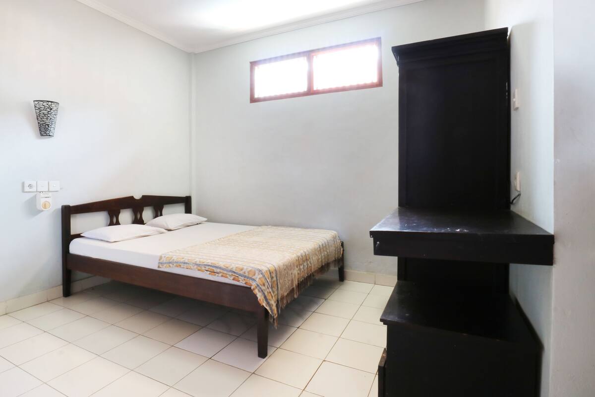 A bedroom with a bed, a window, a wall-mounted TV, and a small shelf.