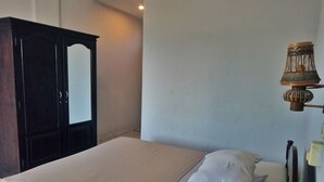 A bedroom with a bed, a wooden wardrobe, and a wall-mounted lamp. - Taman Mekar Beach Inn (Kuta)