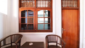 A room with a wooden door, a window with a wooden frame, and two wooden chairs and a small table. - Taman Mekar Beach Inn (Kuta)