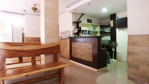 A reception area with a wooden bench, a reception desk, a fan, and a TV mounted on the wall. - Taman Mekar Beach Inn (Kuta)