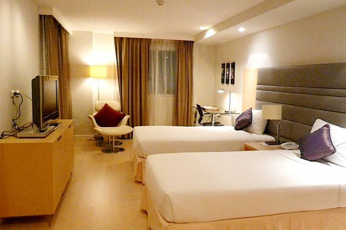 Une chambre d’hôtel avec deux lits, un bureau, une chaise, une télévision et une fenêtre avec des rideaux.
