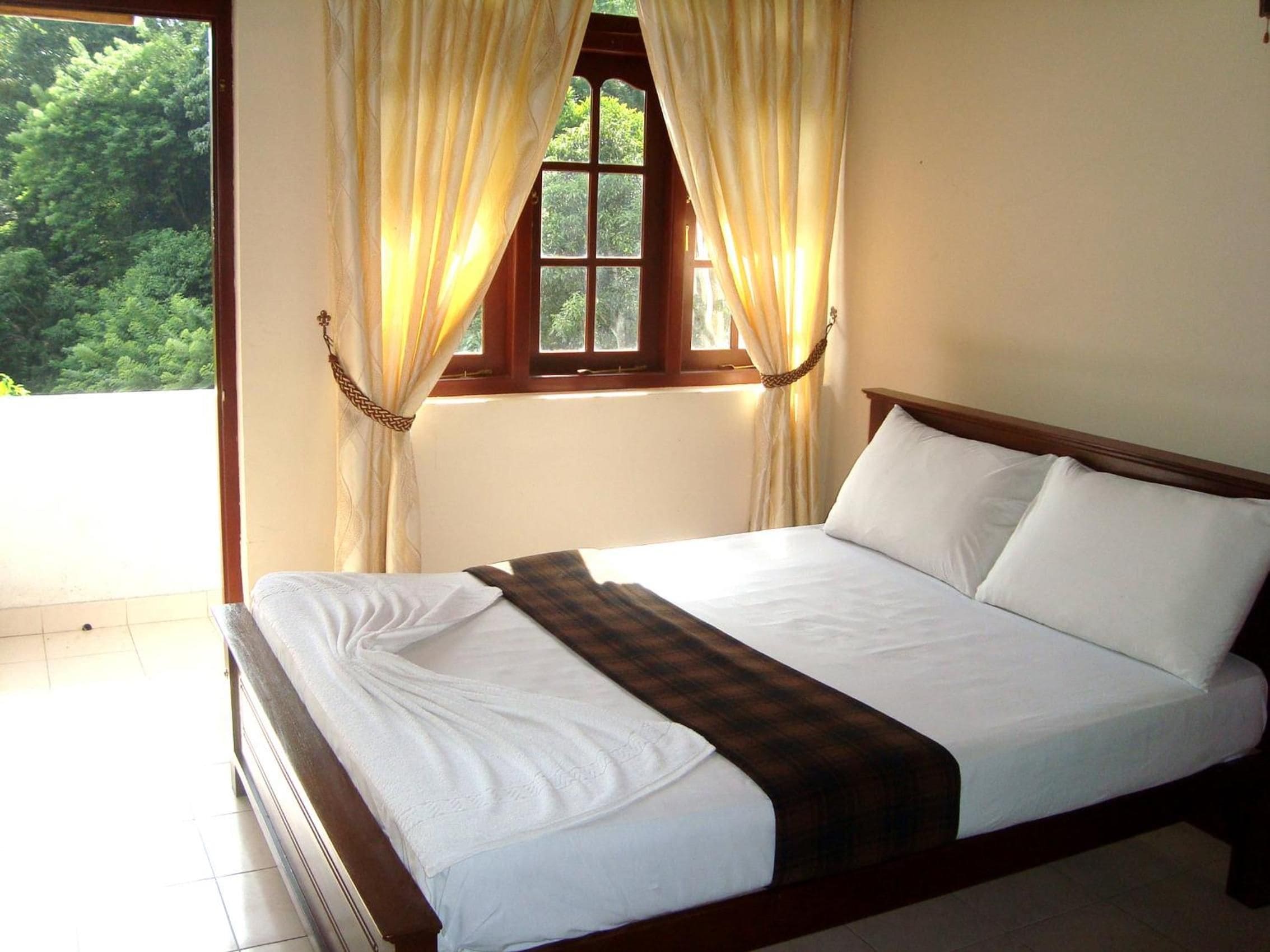 A bedroom with a bed, curtains, a window, and a view of greenery outside.