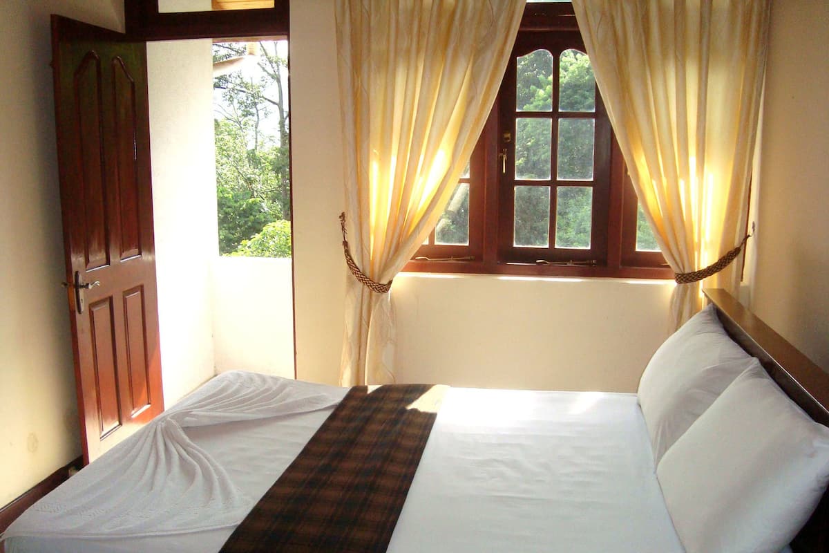 Una cama con sábanas blancas, un edredón a cuadros y una ventana con cortinas.