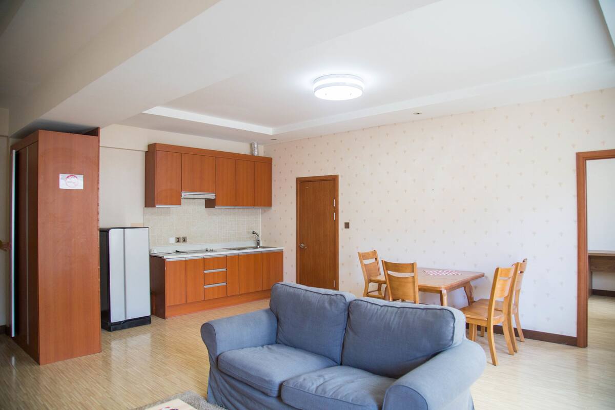 Un espacio habitable compacto con kitchenette, un sofá, una mesa de comedor con sillas y una puerta que da a otra habitación.