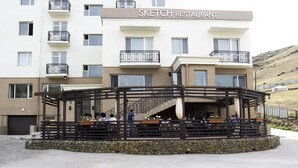 A Sketch Restaurant with outdoor seating, a stone facade, and a multi-story building in the background. - Mount Bogd Apartment (Ulaanbaatar)