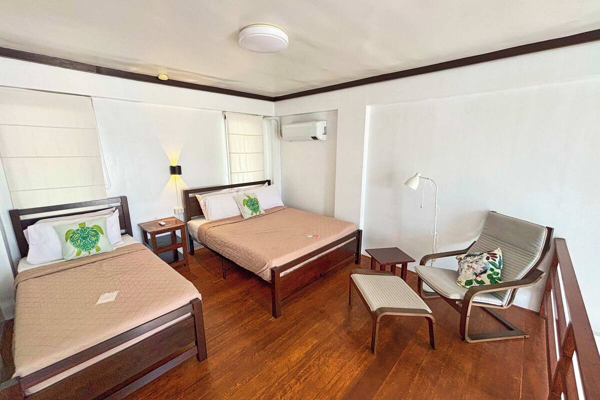 A hotel room with two single beds, a wooden floor, a desk with a chair, and a window with curtains.