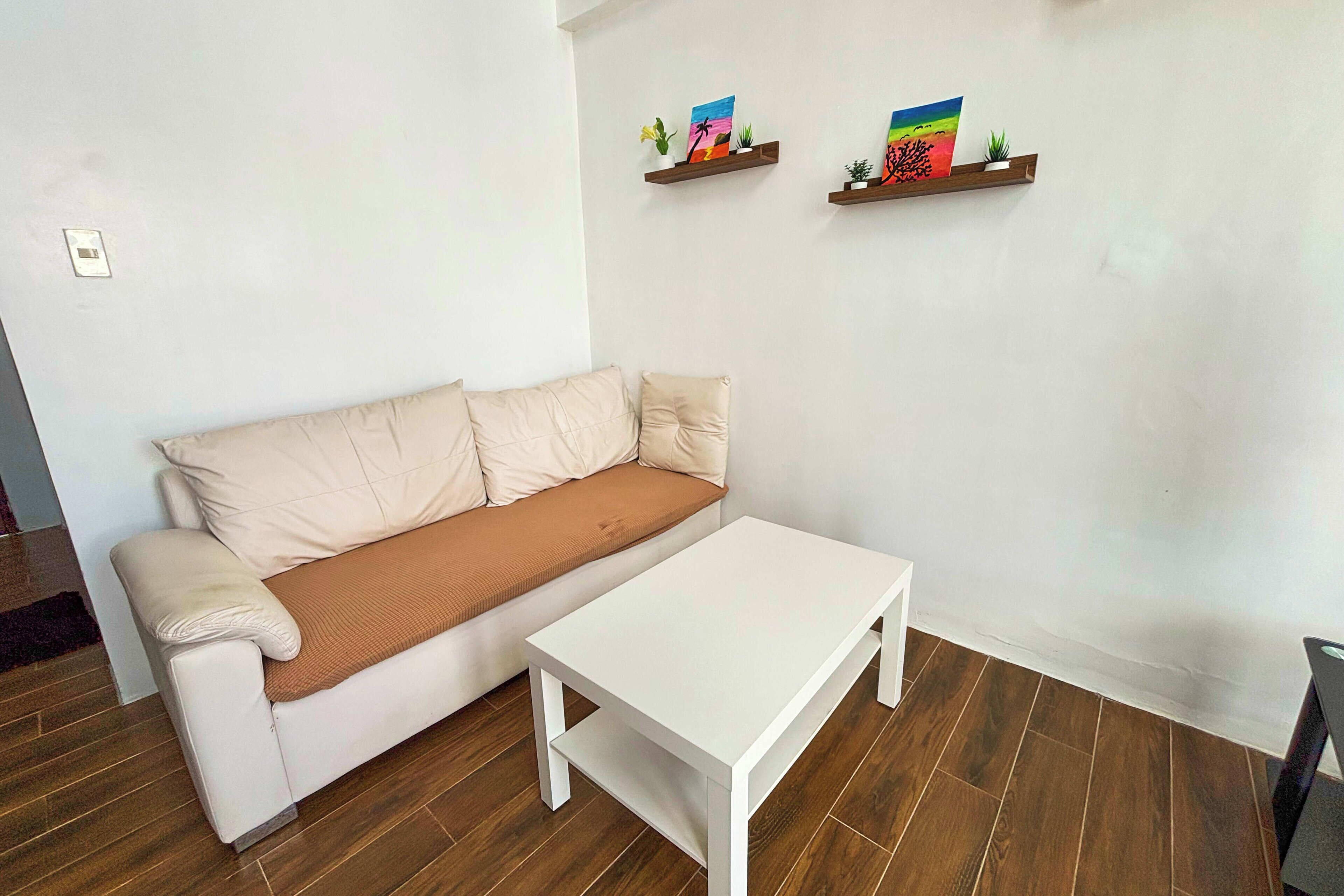 A living room with a beige sofa, a white coffee table, and two wooden shelves with colorful artwork.