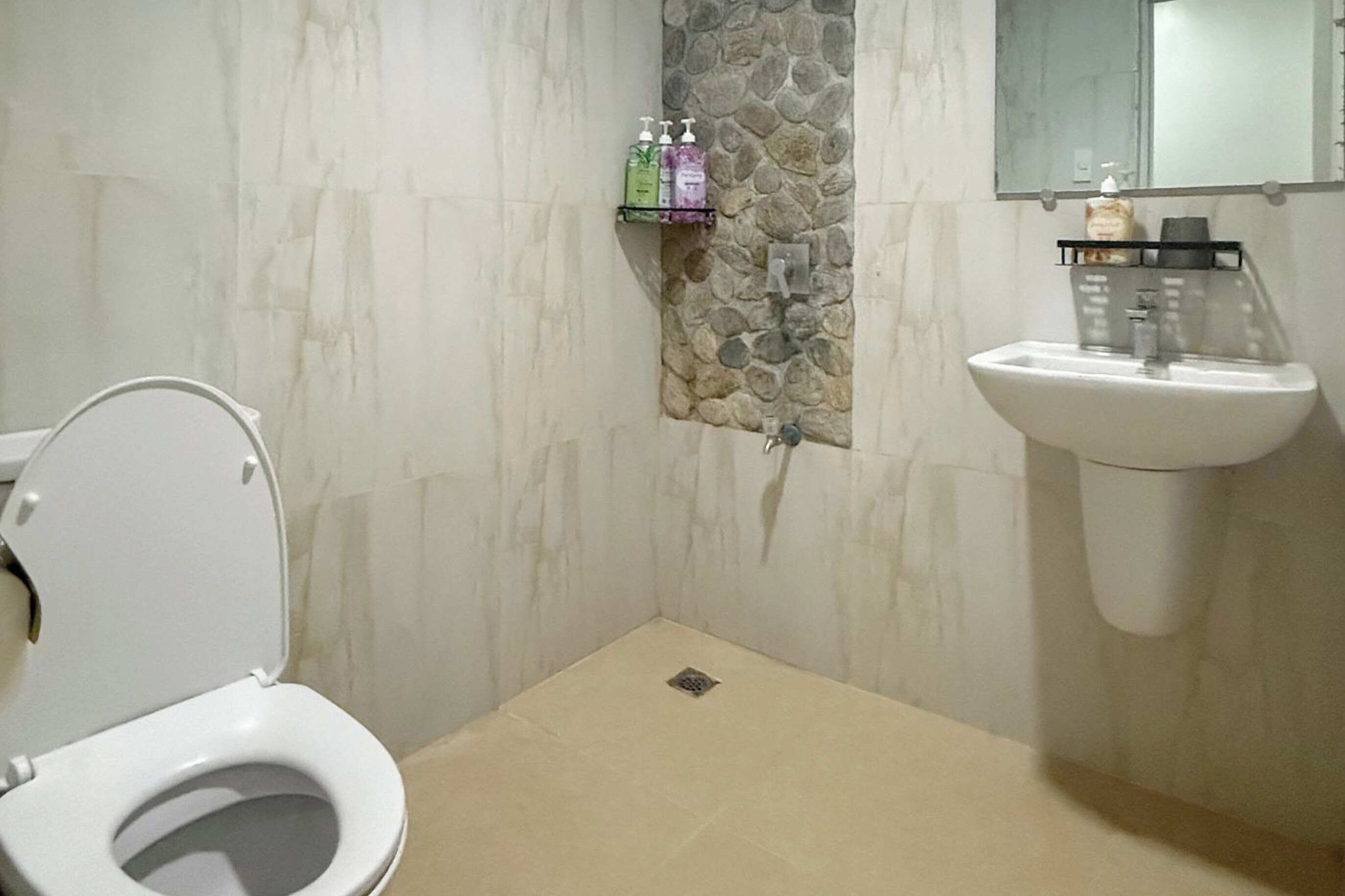 A bathroom with a toilet, sink, and stone wall.