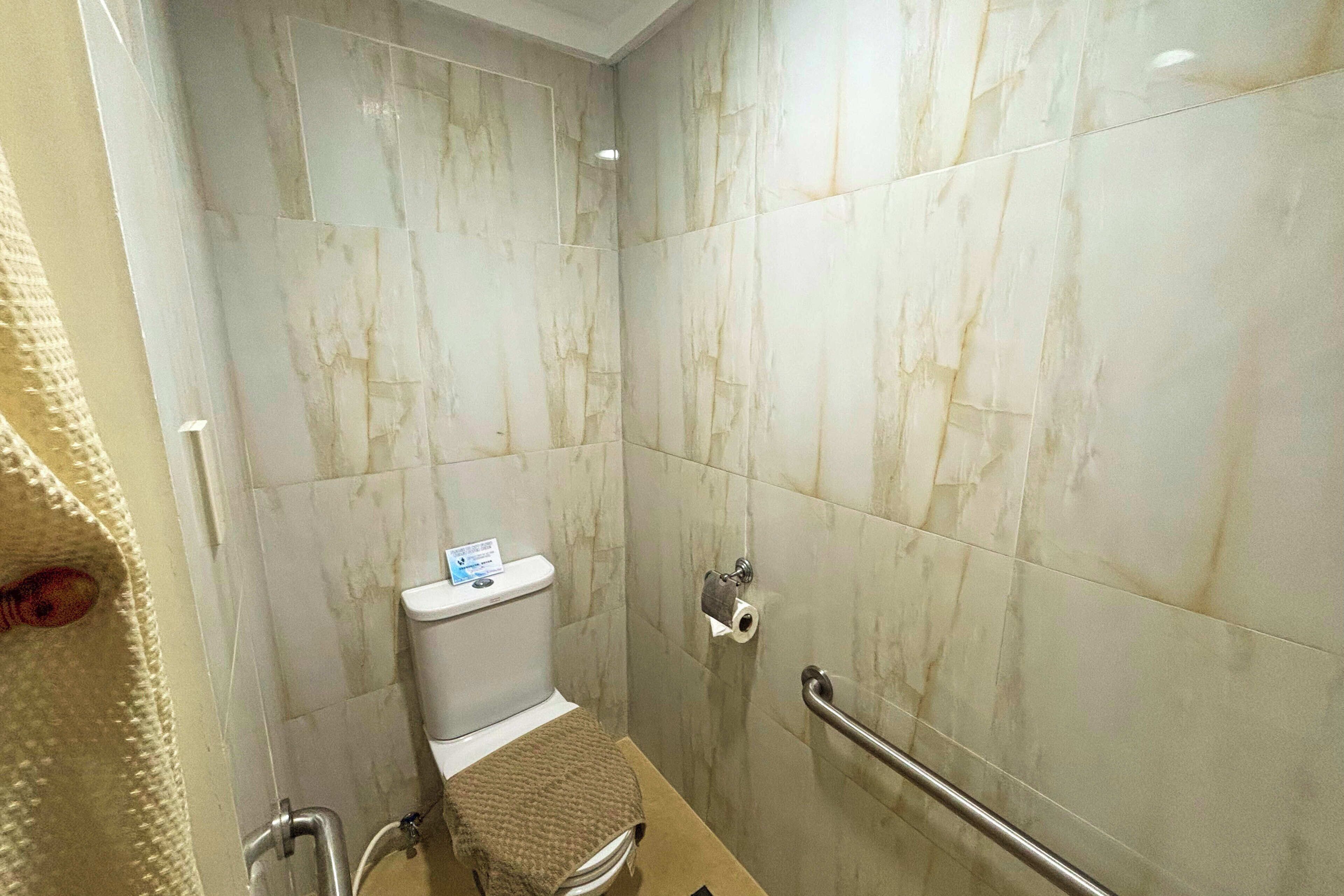 A bathroom with a toilet, a handrail, and a towel rack.