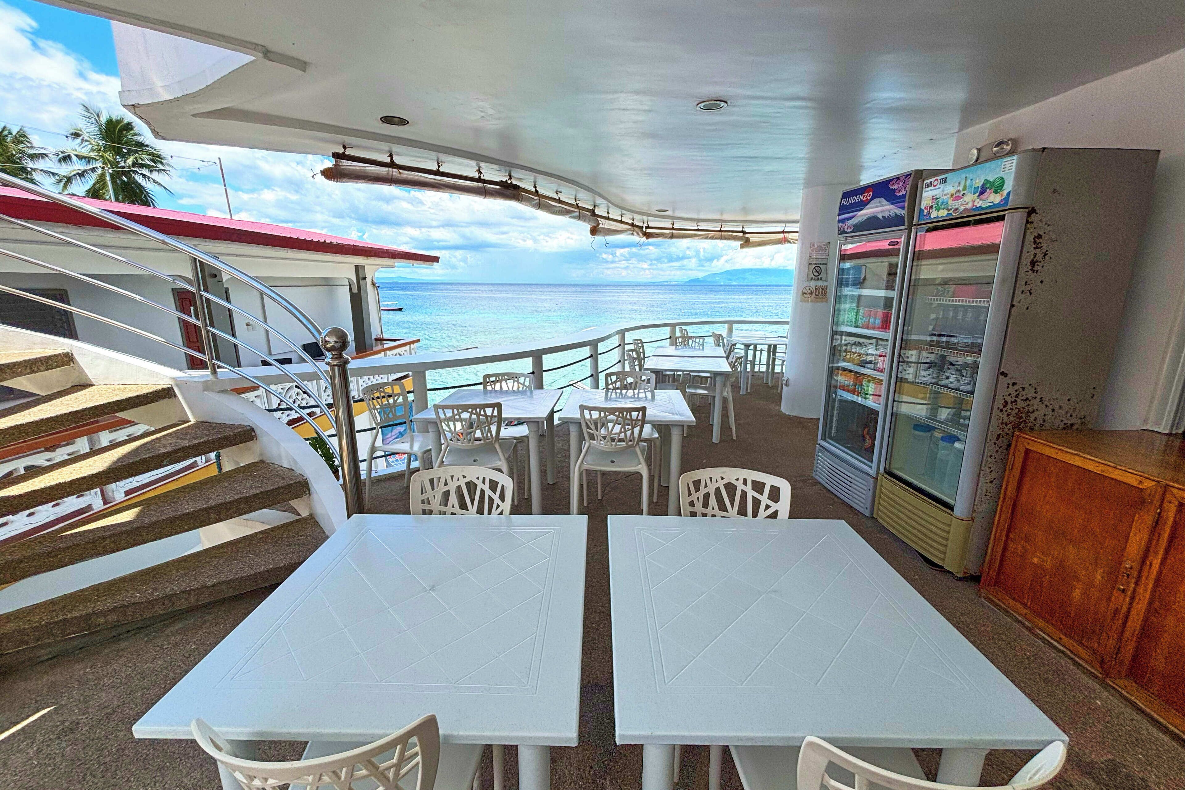 Un restaurant avec des tables et des chaises blanches, un réfrigérateur et une vue sur l’océan.