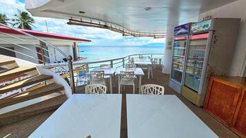 Un restaurant avec des tables et des chaises blanches, un réfrigérateur et une vue sur l’océan.