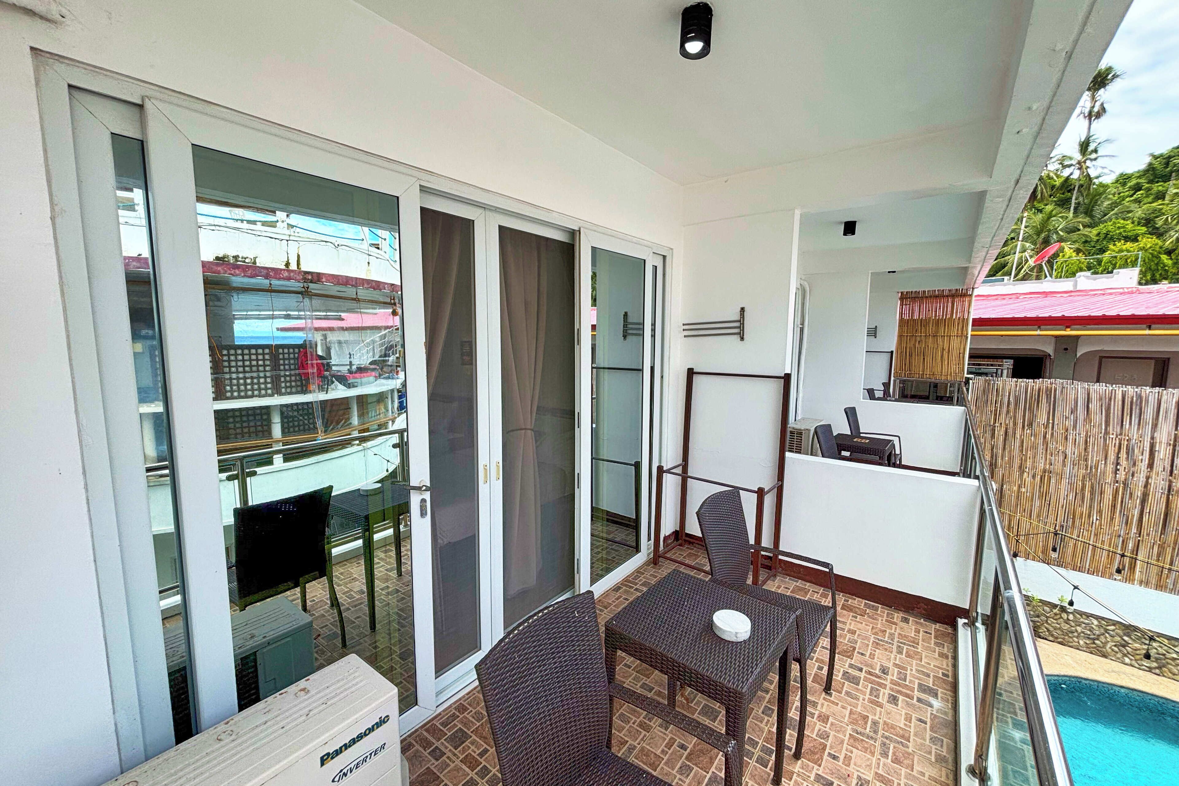 A balcony with a table and chairs, a sliding glass door, and a view of a building with a red roof.