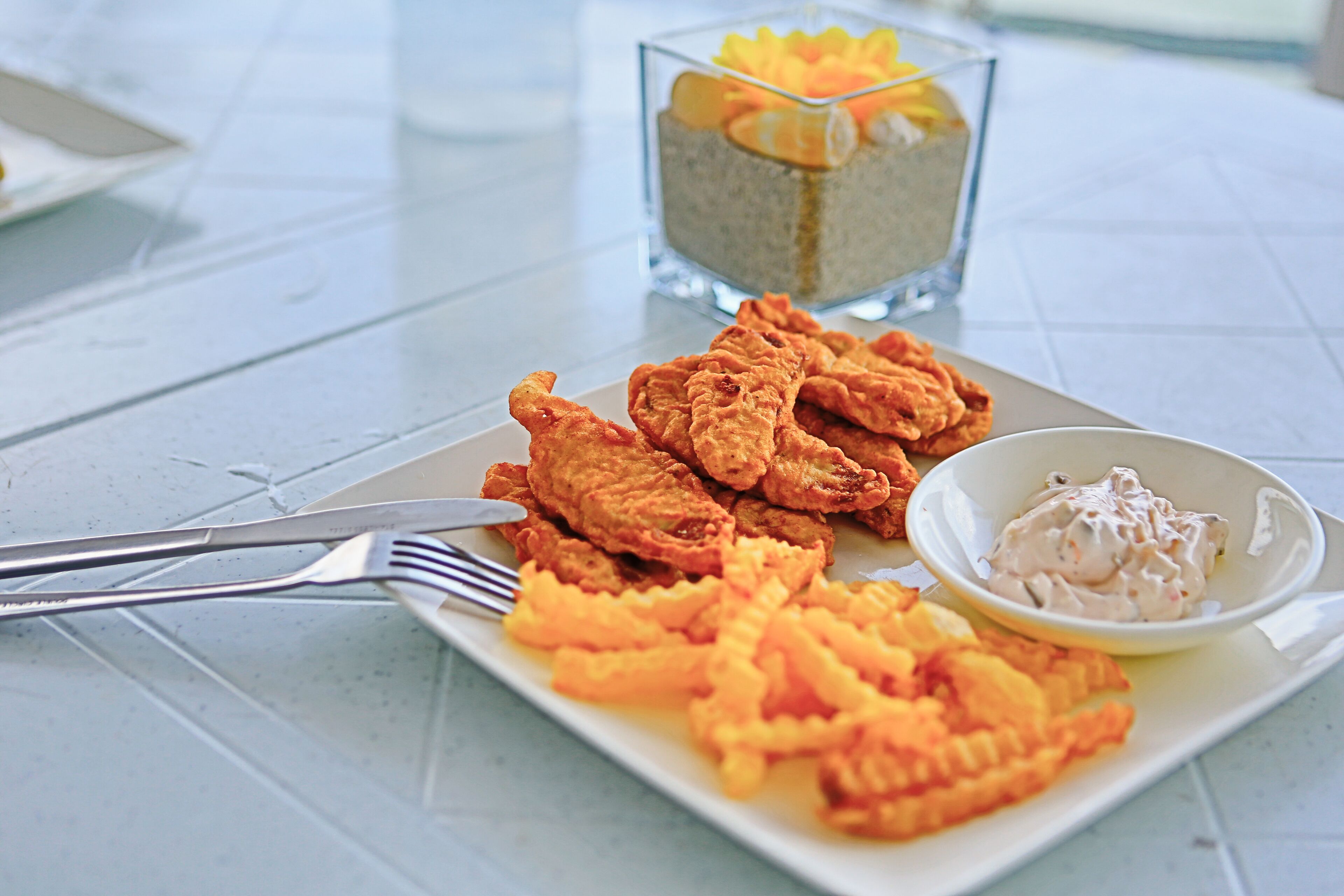 A plate of fried chicken and fries with a small bowl of sauce, on a white table.