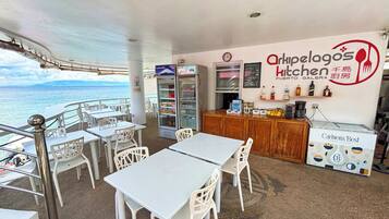 A restaurant with outdoor seating overlooking the sea, featuring a menu board, refrigerators, and a coffee station.