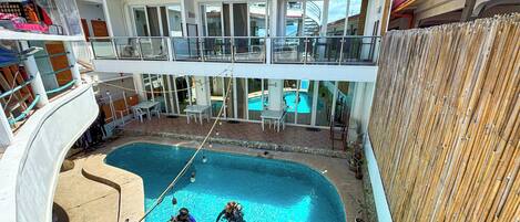A pool area with three people in the water, a covered seating area, and a view of the ship's deck.