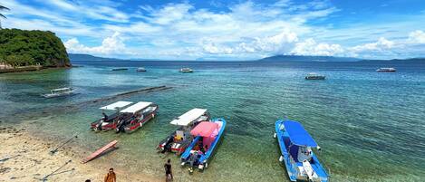 A beach with boats docked, clear water, and a distant mountain.