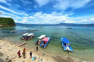 Una playa con barcos amarrados, agua cristalina y una montaña a lo lejos.