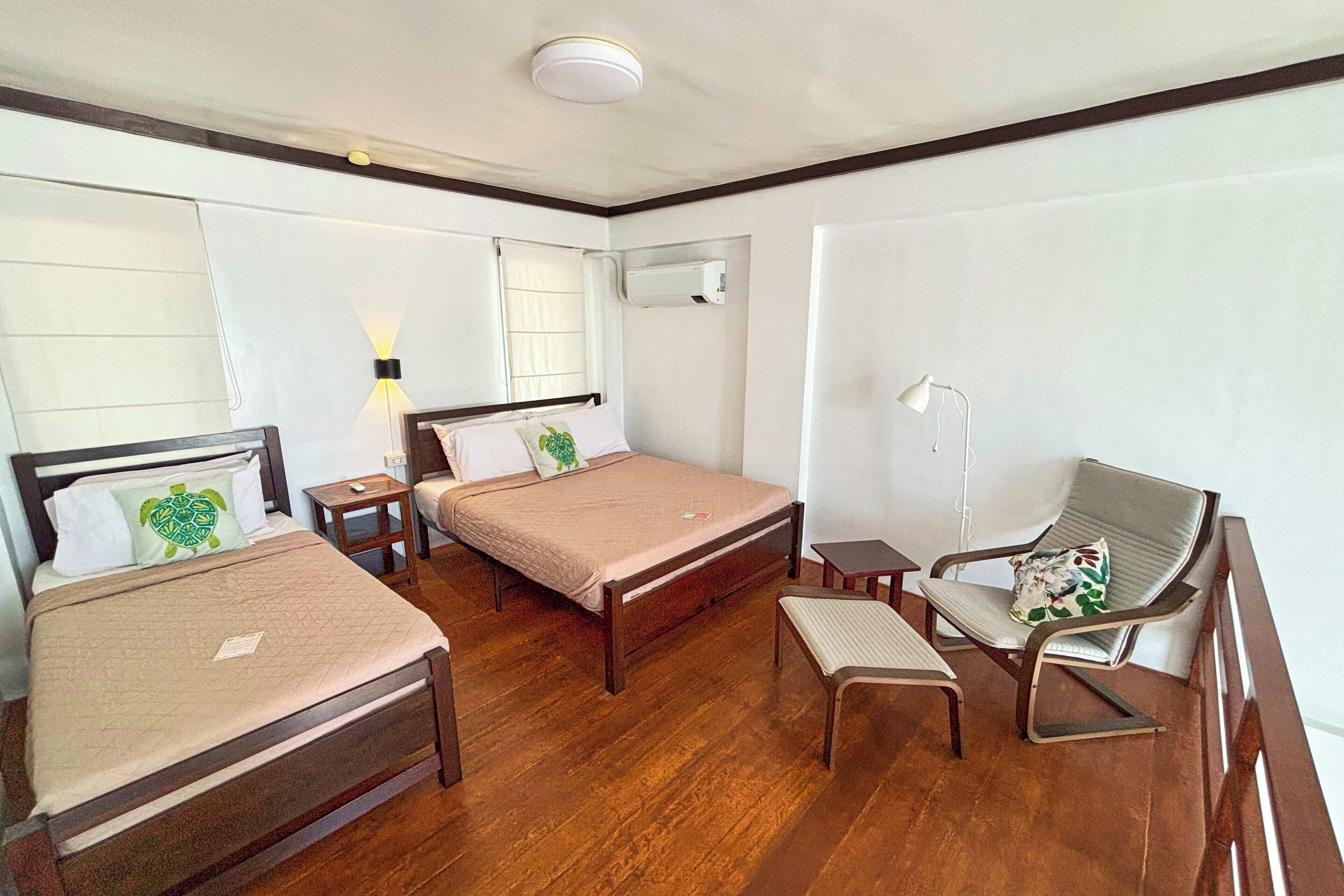 A hotel room with two beds, a desk, a chair, a lamp, and an air conditioning unit.