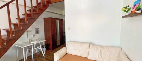 Ein Wohnzimmer mit einem weißen Sofa, einem kleinen weißen Tisch und einer Holztreppe.