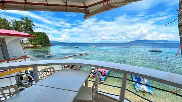 A balcony with a view of the sea, a table, and chairs. - Arkipelago Divers and Beach Resort (Puerto Galera)