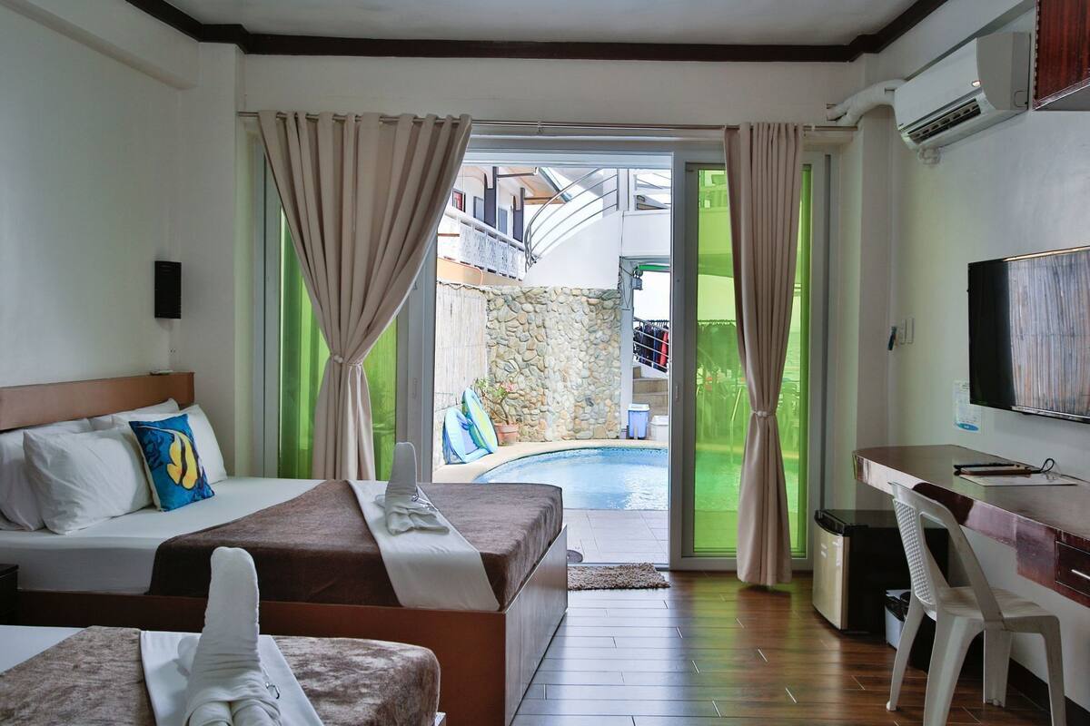 A hotel room with a bed, a desk, a TV, and a view of a swimming pool.