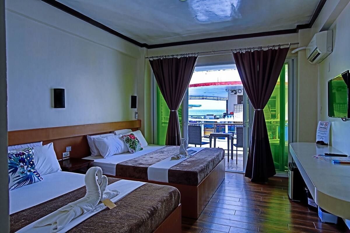 A hotel room with two beds, a desk, a chair, and a view of the sea.