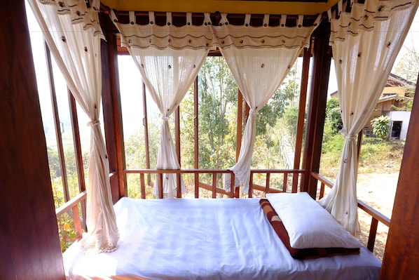 A bed with white linens and a wooden headboard, set in a room with wooden railings and sheer curtains.