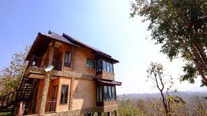 Una casa a due piani con un balcone, circondata da alberi e un paesaggio collinare.