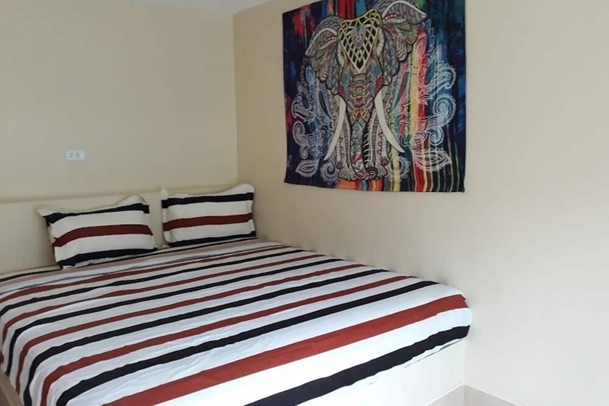Ein Schlafzimmer mit einem Bett, zwei Kissen und einem farbenfrohen, abstrakten Gemälde an der Wand.