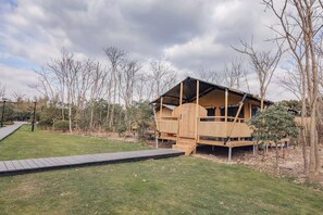 A wooden cabin with a sloped roof, a wooden deck, and a ramp leading to the entrance. - Lin Jia Camping Site Shanghai (Shanghai)