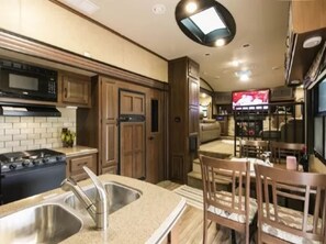 A compact RV kitchen with a stove, sink, and wooden cabinets.