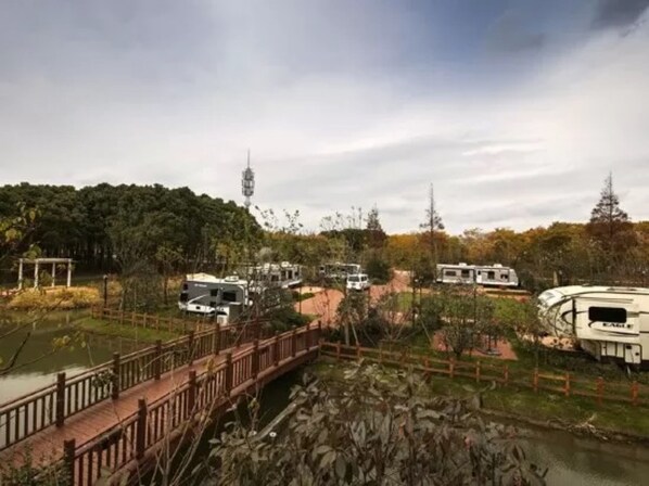 A campground with RVs parked near a bridge over a pond, surrounded by trees and a forested area. - Lin Jia Camping Site Shanghai (Shanghai)