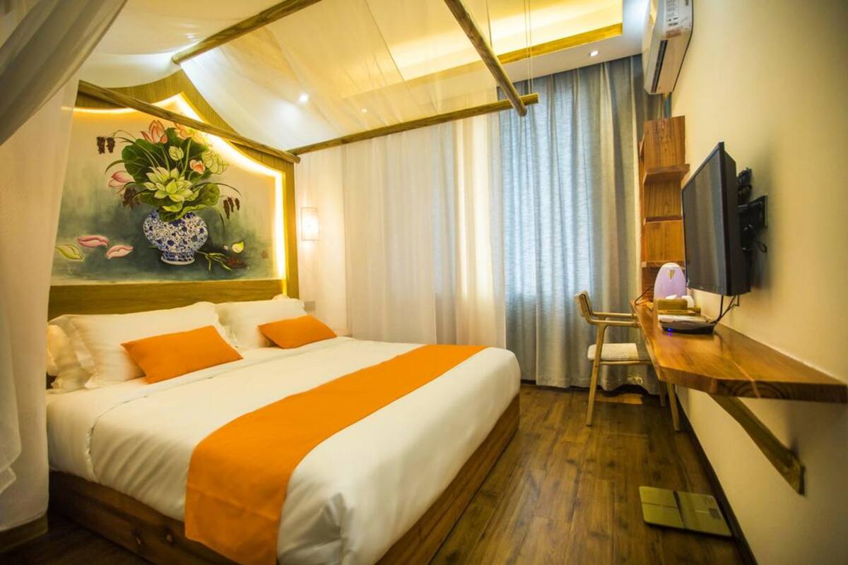 A hotel room with a bed, a desk with a chair, a television, and a painting on the wall.
