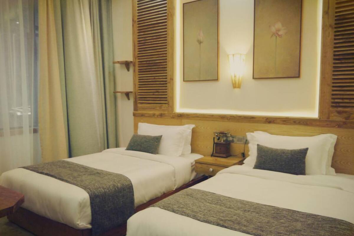 A hotel room with two beds, a nightstand, a lamp, and a window with curtains.
