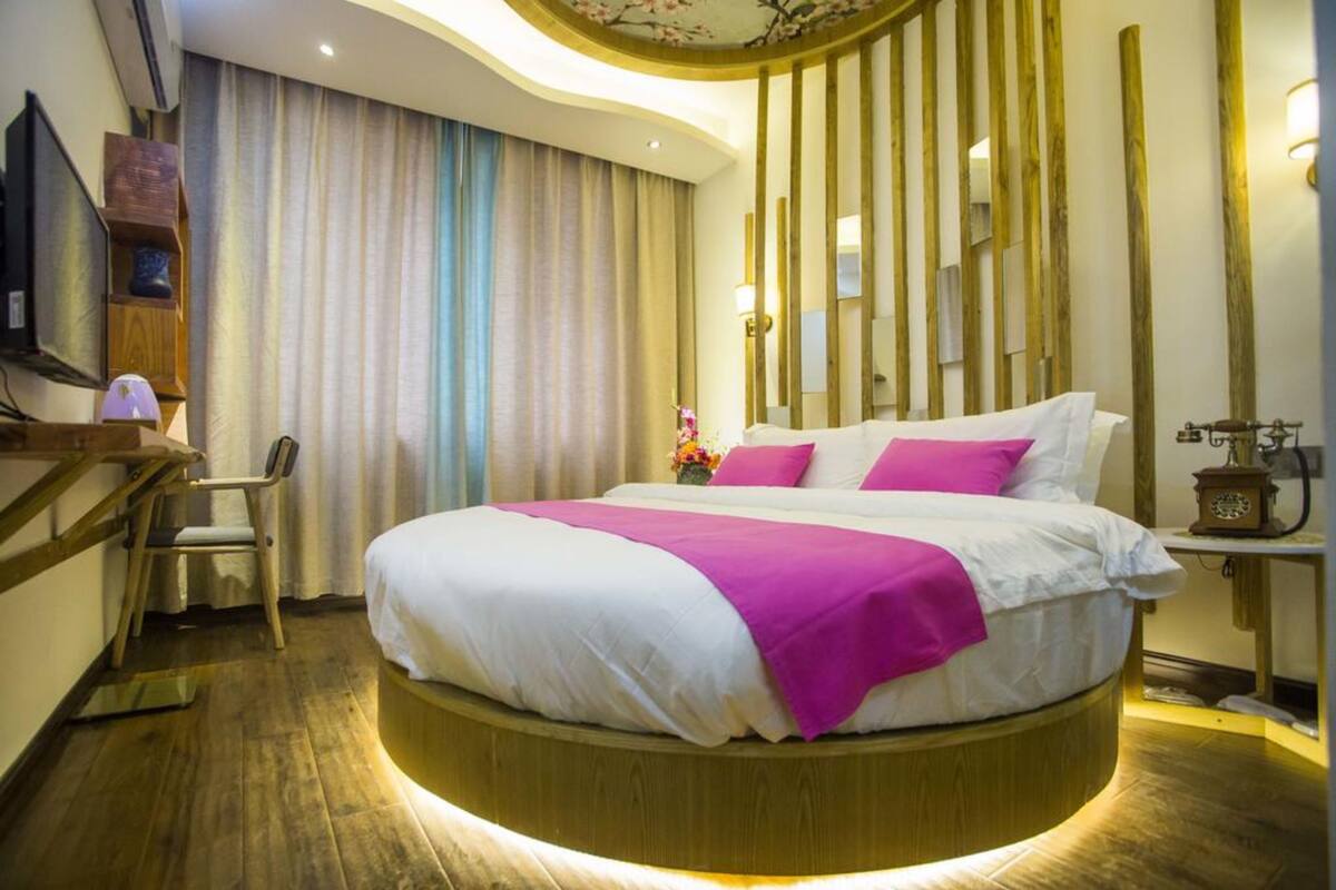 A circular bed with a white and pink bedspread, a wooden headboard, and a bedside table with a lamp.